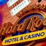 Close-up of a Hard Rock Hotel & Casino neon sign featuring a guitar shape against a bright blue sky